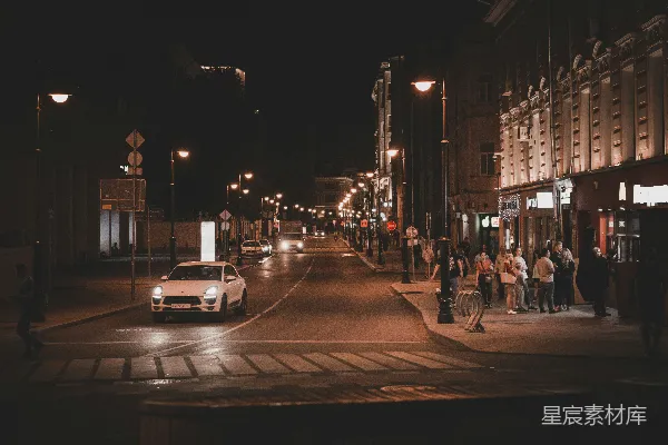 夜晚路上车辆稀少，人们在建筑物附近行走。