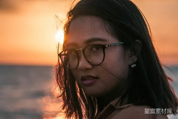 穿着黑色框架太阳镜的女人在海滩上欣赏日落。