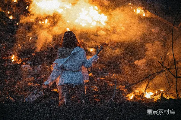 穿着白色衬衣的女人站在一堆火旁边
