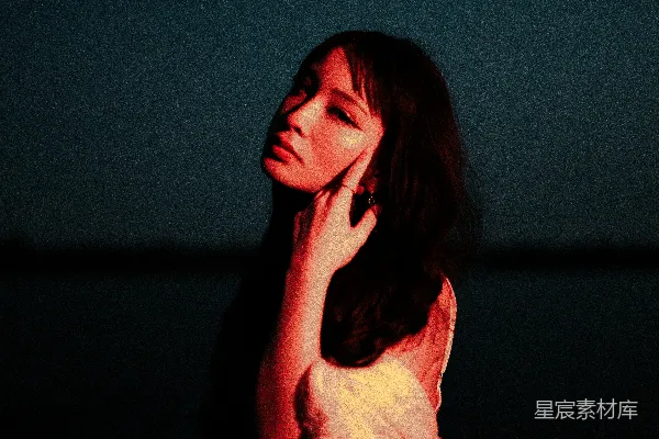 一个女人站在黑暗中，用手捂住脸。
