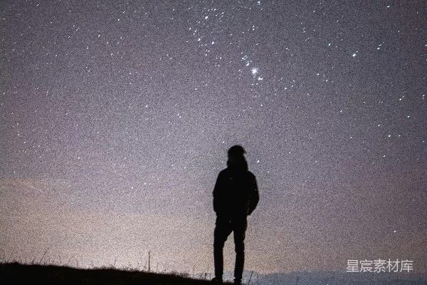 山上有人站立眺望夜空中的星星。