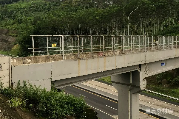 高清摄影 一座横跨高速公路的行人桥，桥的两侧是被树木覆盖的小山。