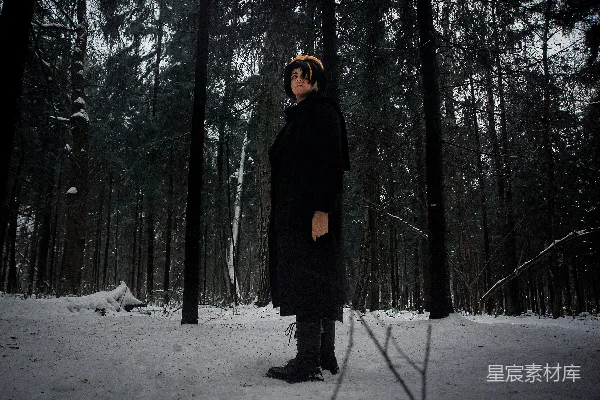 穿着黑色大衣的人站在雪林中