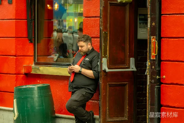 一个男子靠在一幢红色建筑旁边，“Temple Bar”招牌就在他身后。