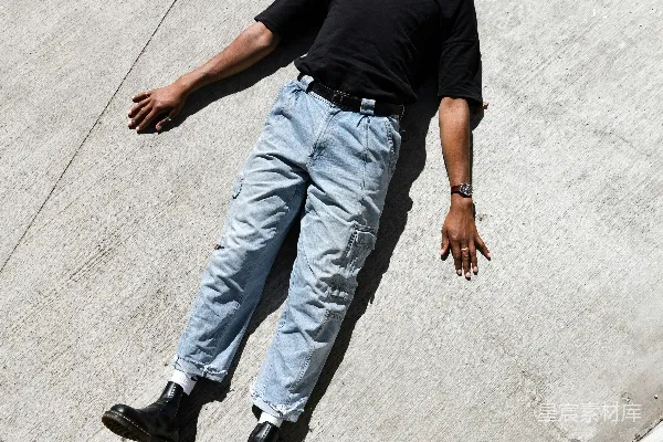 高清摄影 一个穿着黑色T恤和蓝色牛仔裤的男人在白天走在灰色混凝土地板上。
