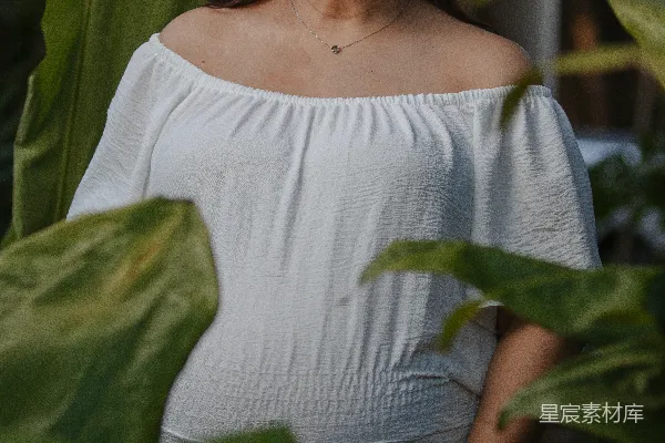 一个微笑的孕妇在户外穿着白色服装。