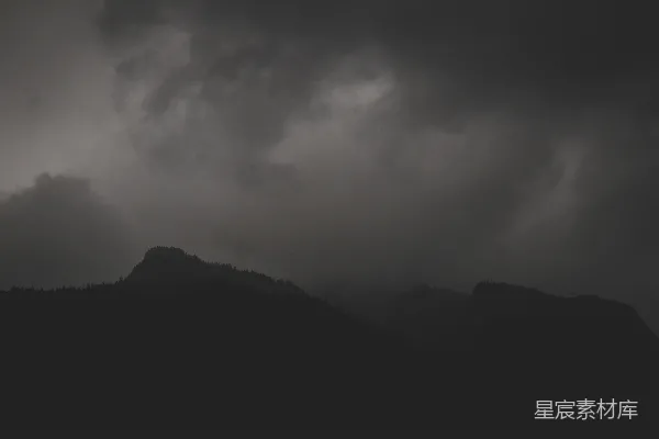 一张黑白照片，山峦下云层密布的天空。