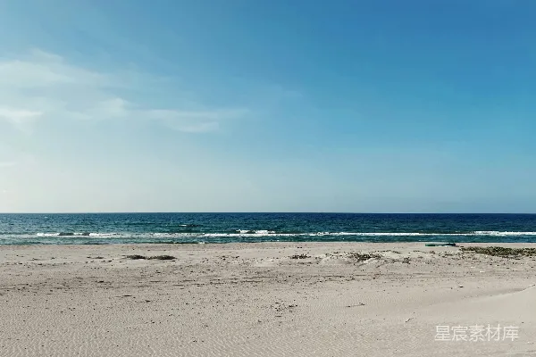 海边的一片沙滩靠近大海，天空湛蓝。