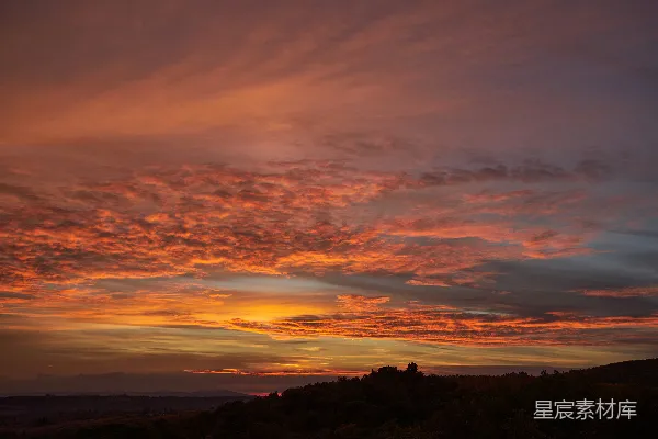 壮丽的夕阳天空中燃烧着的云彩映照在起伏的山丘上。