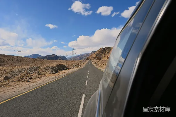 一辆车在沙漠小道上行驶，背景是山峦。