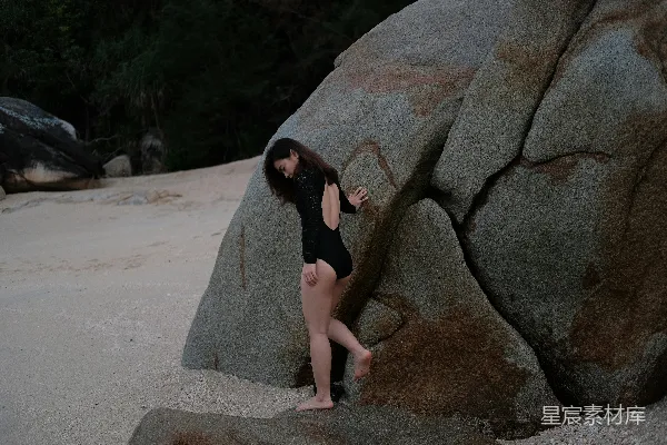 一个穿泳衣的女人站在一块大石头旁边