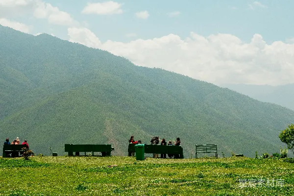 人们聚集在一片草坡上，背景是山峦。