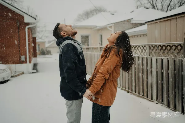 黑夹克的男人和棕色风衣的女人站在覆盖着白雪的地面上，在白天。