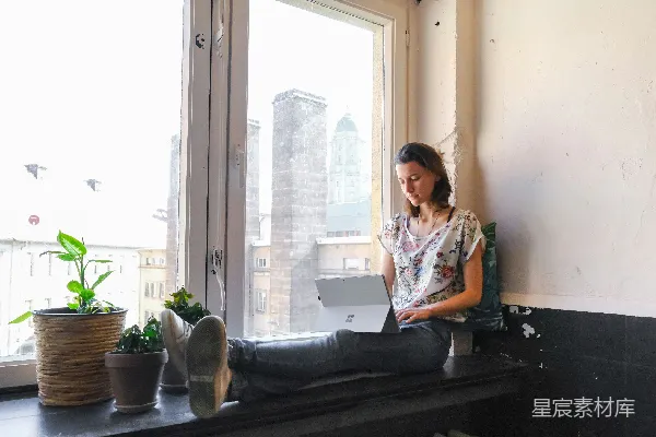 身穿白色和红色花图案上衣的女子坐在窗边。