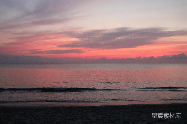 海边平静的海面上升起的粉红色云霞
