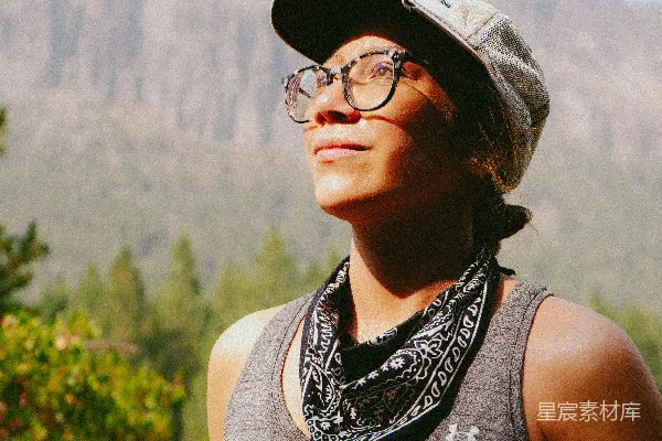 一个戴帽子和眼镜的女人站在山前。