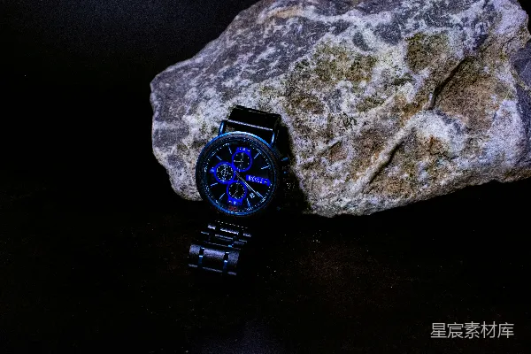 一块手表旁边放着一块岩石在黑色的表面上