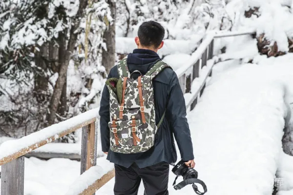 黑色夹克和棕色裤子的男人站在覆盖着积雪的地面上，白天的景象。