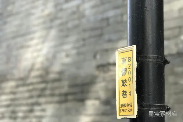 高清摄影 一盏黄色的标志灯挂在黑色的杆子上，背景是一面砖墙。