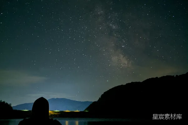 夜晚一个人坐在岩石旁水体附近的轮廓