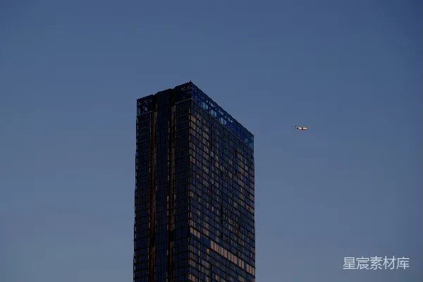 高清摄影 一座非常高大的建筑物，天空中有一架飞机飞过。