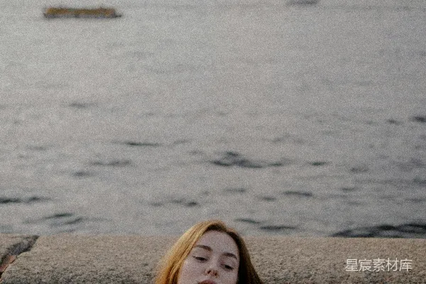 女人靠着一块石头靠近一片水域。