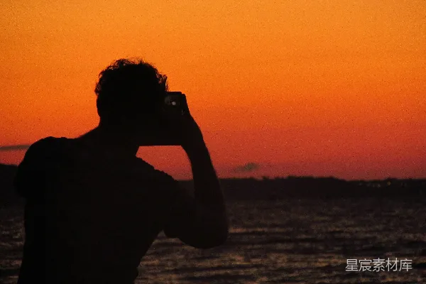 一个男人在夕阳映照下的海边拍照