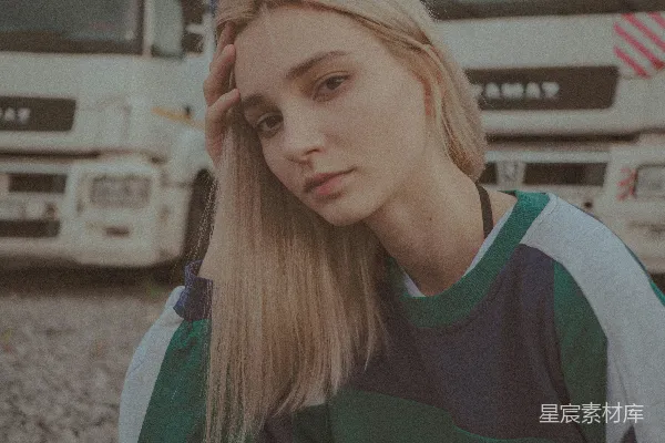 一个金发的年轻女子站在白颜色的卡车前面摆姿势。