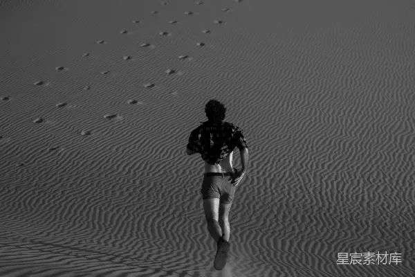 高清摄影 一个男人走过一片沙地，脚印留在沙子里。