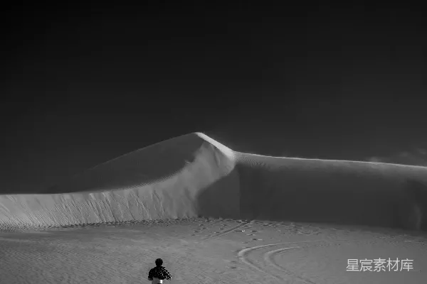 高清摄影 一个男人在昏暗的天空下穿过一片沙地。