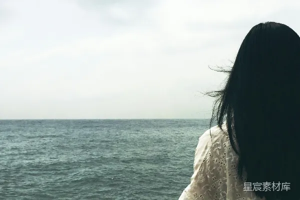 女人面对着一片水域，天空阴沉。