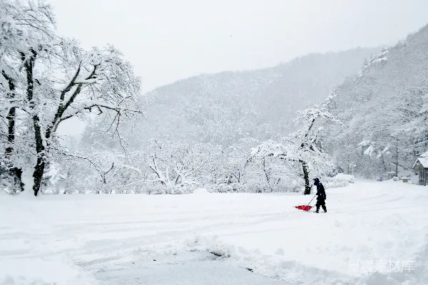 黑夹克红裤子的人坐在红色雪橇上，在覆盖着白雪的地上滑行。