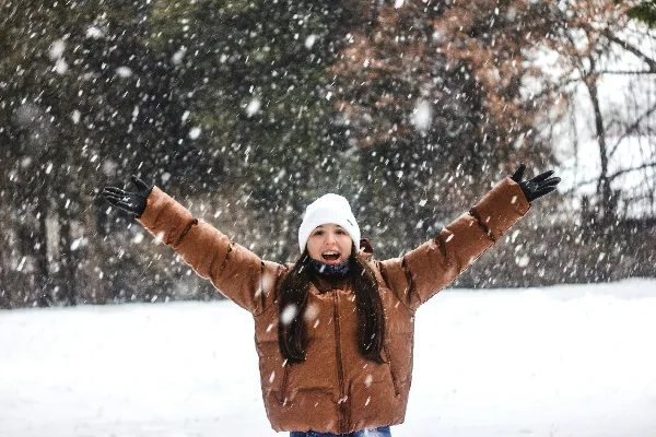 棕色夹克和白色针织帽的女人站在覆盖着积雪的地面上，在白天。
