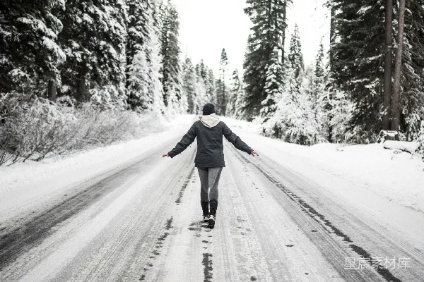 黑色夹克的人在白天走在覆有白雪的道路上。