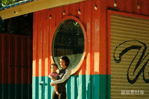 妇女抱着婴儿站在色彩缤纷的海边小屋前。
