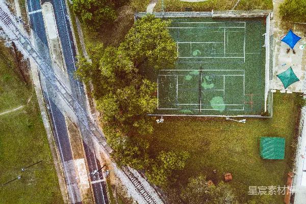高清摄影 高角度拍摄的绿色草坪网球场，周围有树木、道路和铁路。