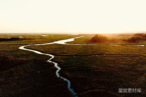 高清摄影 夕阳西下，一条蜿蜒的河流流经一片绿色的沼泽地。