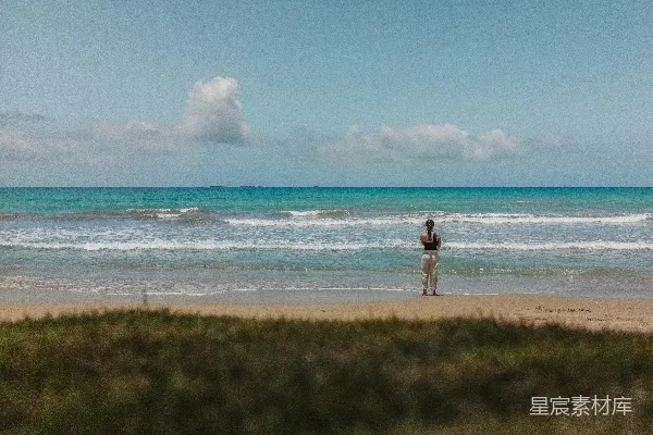 高清摄影 一个男人站在沙质海滩上，旁边是海洋。
