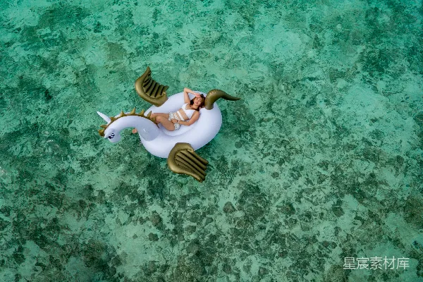 高清摄影 穿着白色比基尼套装的女人躺在白色的棕色独角兽充气浮床。
