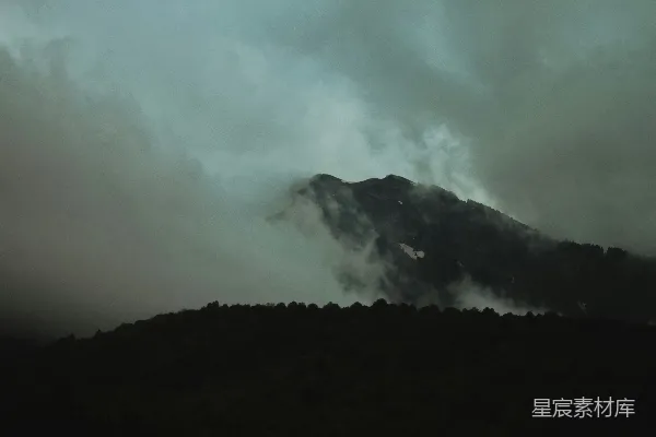 高清摄影 一座被云雾笼罩的山，背景是黑暗的天空。