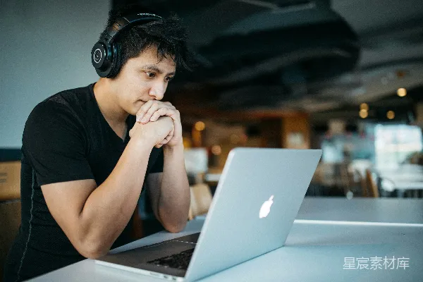 高清摄影 一个戴着耳机的男人坐在椅子上，面前有一台MacBook电脑。