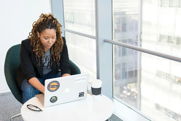 高清摄影 白天，一位女性坐在带垫的椅子上使用MacBook电脑。