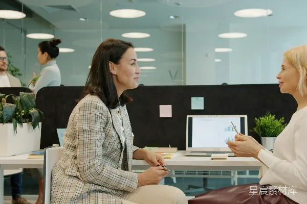 高清摄影 两位女士在办公室的桌子旁交谈。