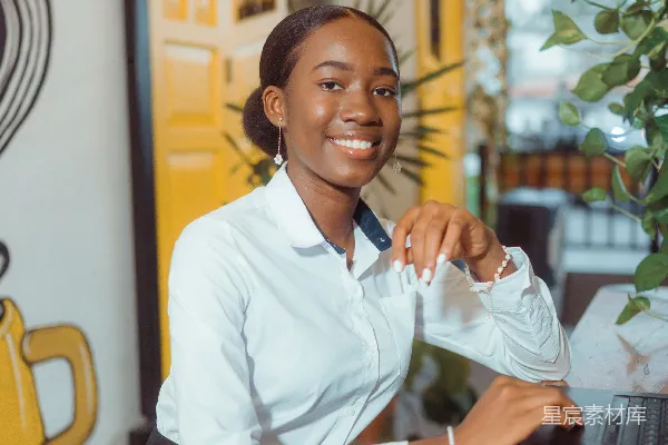 高清摄影 一位穿着白色衬衫的微笑女性在一台笔记本电脑前。