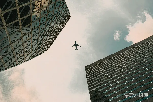 高清摄影 一架飞机在多云的天空中飞过现代化摩天大楼之间。