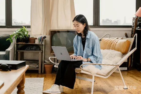 高清摄影 穿蓝色衬衫的女人坐在白色椅子上使用Surface笔记本电脑。
