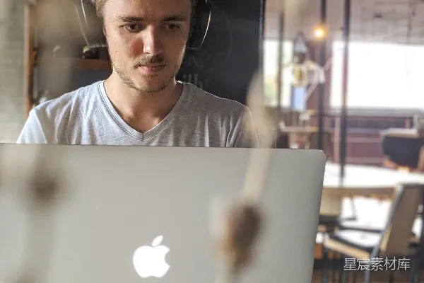 高清摄影 穿着灰色V领衬衫的男人站在苹果MacBook面前。