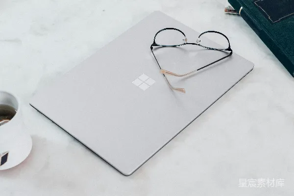 高清摄影 银色的Microsoft Surface Laptop 3在白色桌面上，旁边放着一副黑色框架的眼镜。