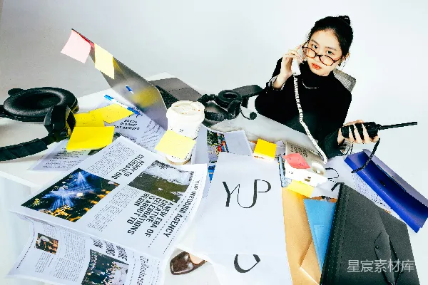高清摄影 正在凌乱的书桌前打电话的女人，书桌上散落着文件和笔记本电脑。