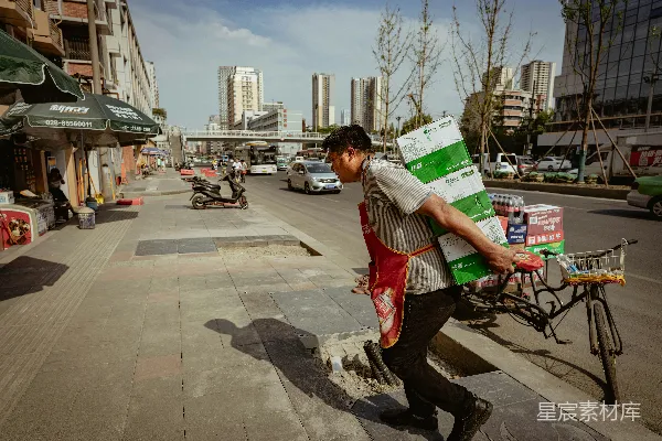 高清摄影 穿红色背心和黑色裤子的男人手里拿着一个白色和绿色的盒子。